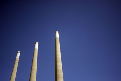 Low angle view of smoke emitting from chimney against clear blue sky