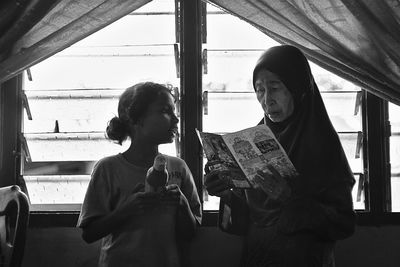 Girl with grandmother against window at home