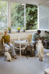 Man and woman sitting on chairs while waiting with dogs in animal hospital