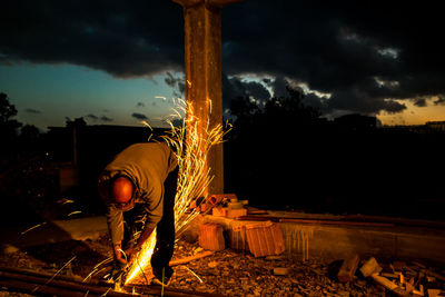 Worker cutting metal against cloudy sky at dusk