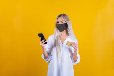 Young woman using smart phone against yellow background