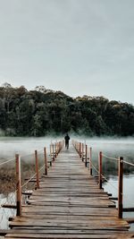 Rear view of woman on footbridge against sky