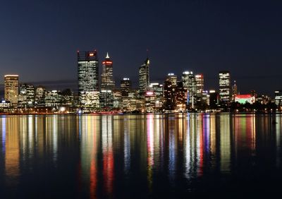 Illuminated buildings by river against sky at night