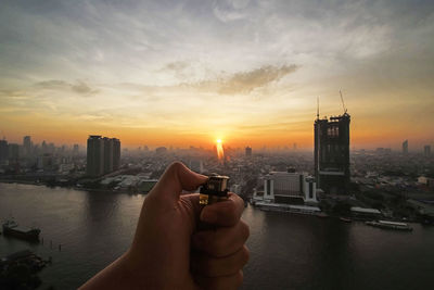 Midsection of man holding river against buildings in city at sunset