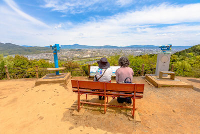 Rear view of couple sitting on mountain against sky