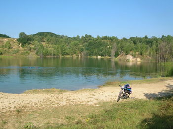 Man riding bicycle by lake against clear sky