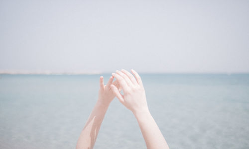 Cropped hands against sea at beach during summer