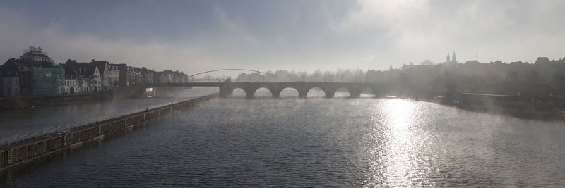 Bridge over river in city against sky