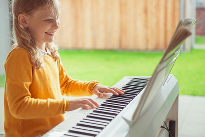 Side view of girl playing piano while sitting at home