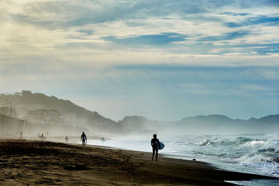 People on beach against sky during sunset