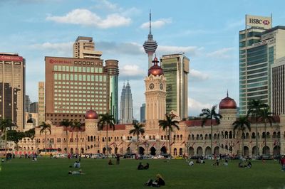 People at lawn by sultan abdul samad building with skyscrapers in city