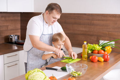 Father son are preparing fresh vegetables in kitchen. dad and boy child cut