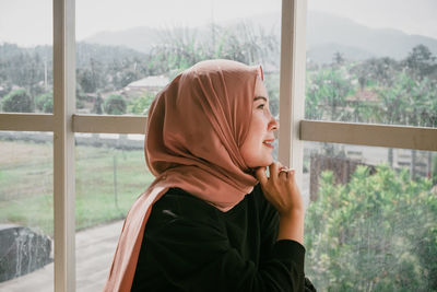 Portrait of young woman looking through window