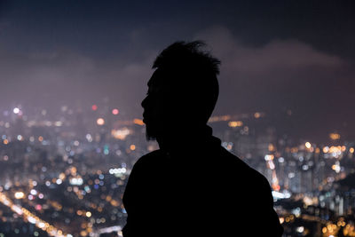 Rear view of silhouette man against illuminated city at night