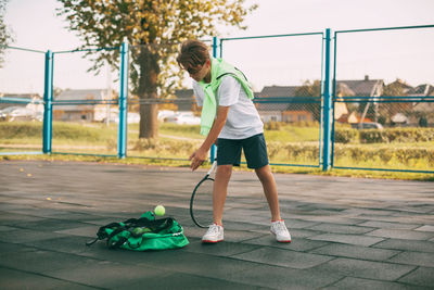 A young athlete takes a ball from a sports bag, holds a tennis racket in his hand 