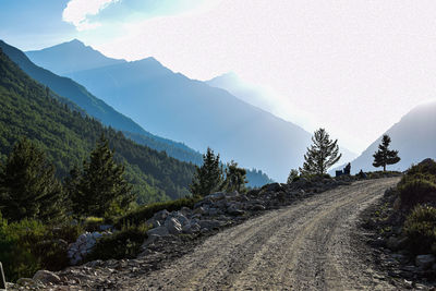 Dirt road by mountains against sky
