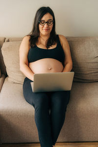 Young woman using laptop while sitting on sofa at home