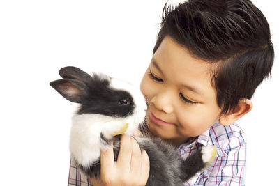 Close-up of smiling boy holding rabbit against white background