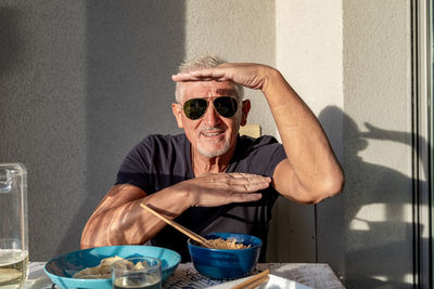 Attractive middle-aged man have fun while eating sitting on table laid chinese food in front of wall