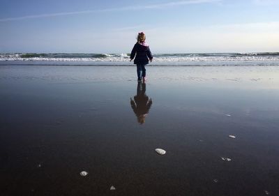 Rear view of girl on beach against sky