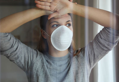 Young woman wearing flu mask looking away standing at home