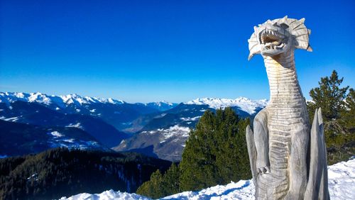 Statue against snowcapped mountains against clear blue sky