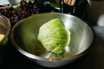 Crisp iceberg lettuce head in a stainless steel bowl on a modern kitchen countertop.
