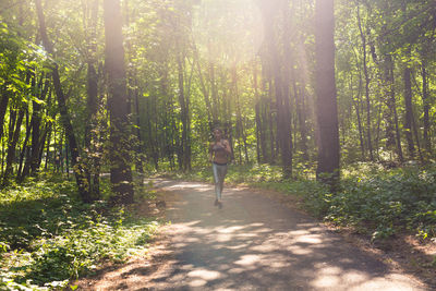 Rear view of woman walking on road amidst trees in forest