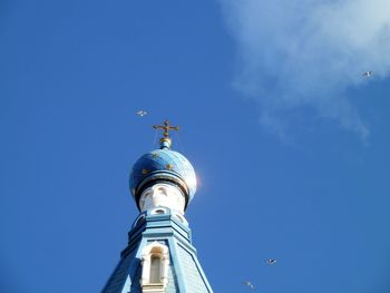 Low angle view of cross amidst buildings against blue sky