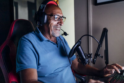Smiling senior man wearing headphones using keyboard while playing video game at home