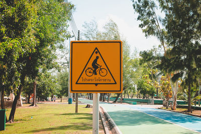Road sign by trees against sky