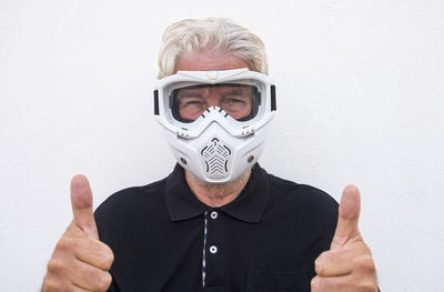 Portrait of senior man wearing mask standing against wall