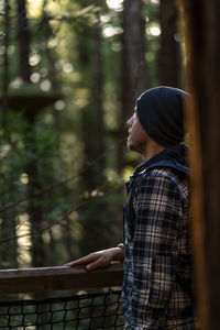 Side view of young man standing against trees in forest