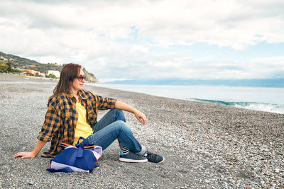 Woman in warm plaid shirt resting and watching sea on winter beach. traveling. wellbeing and harmony