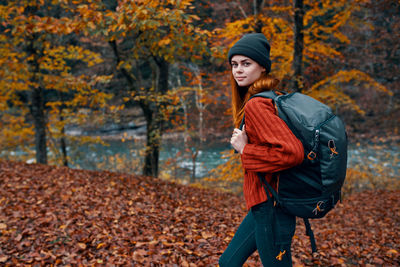 Portrait of young woman standing by autumn leaves