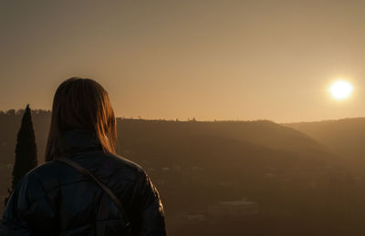 Rear view of woman standing on landscape against sunset sky