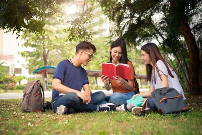 Friends looking at book while sitting on field