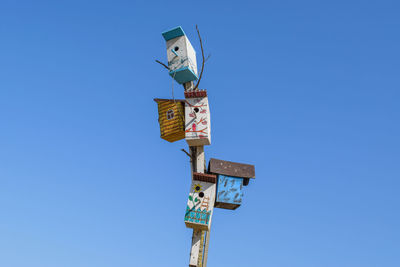 Low angle view of birdhouses on pole against clear blue sky