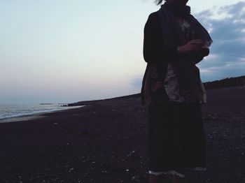 Woman standing on beach against sky during sunset