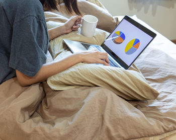 Midsection of man holding coffee while sitting on bed at home