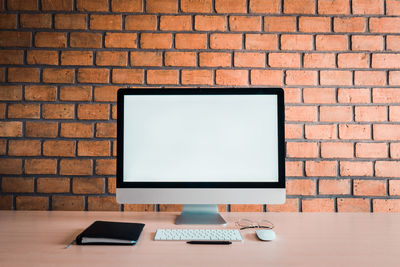 Low angle view of laptop on table against brick wall