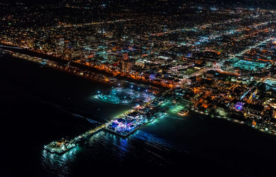 Aerial view of sea by illuminated cityscape at night
