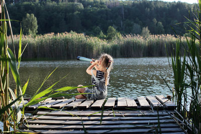 Rear view of girl sitting on pier over lake