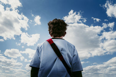 Low angle rear view of boy standing against cloudy sky