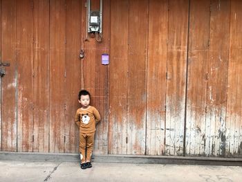 Boy standing against wooden wall