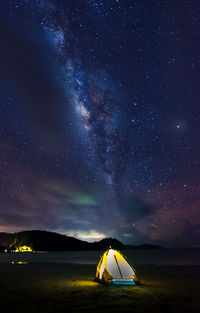 Illuminated tent on beach against sky at night