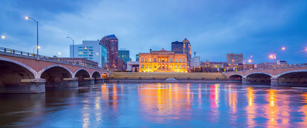 Bridge over river by illuminated buildings against sky