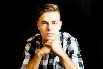 Portrait of handsome man with hands clasped against black background