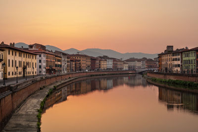 Bridge over river by buildings against sky during sunset