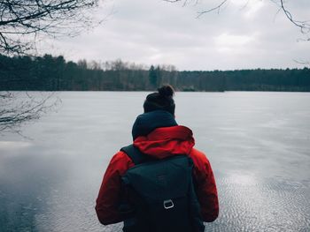 Rear view of mid adult man with backpack standing by frozen lake against sky